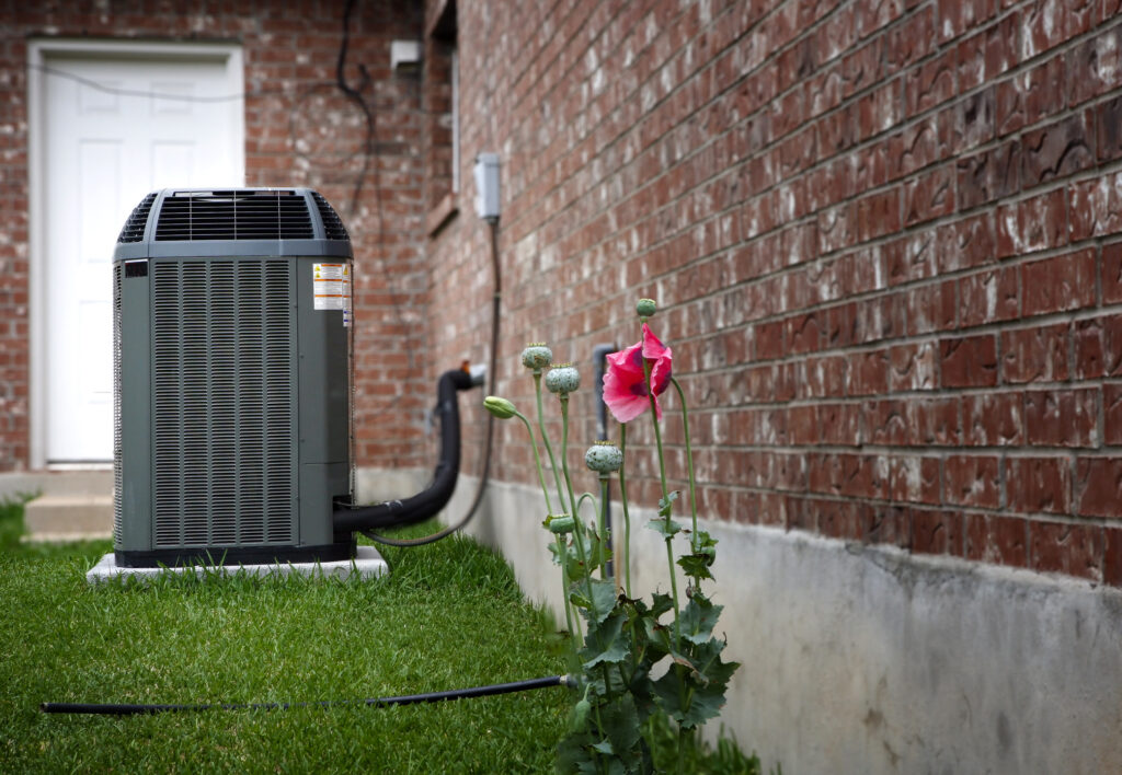 High-efficiency modern HVAC unit installed outside a brick home. Pink flowers in foreground.